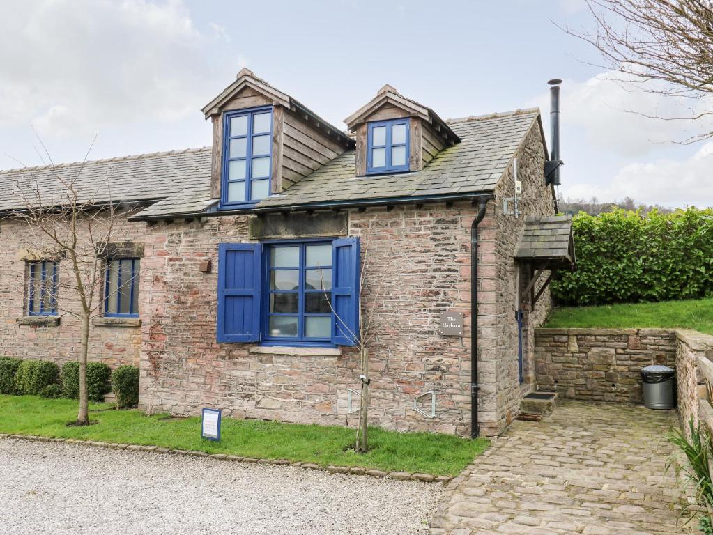 an old brick house with blue windows and a driveway at The Hay Barn in Disley