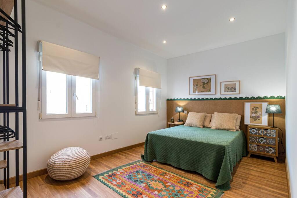 a bedroom with a bed with a green bedspread and two windows at Piso céntrico San Simón in Santander