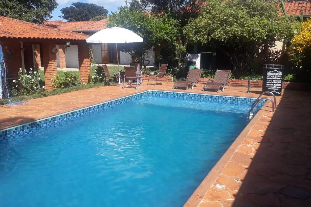 a blue swimming pool with chairs and an umbrella at Chácara Sossego do Vovô, Cond Vitassay - Boituva in Boituva