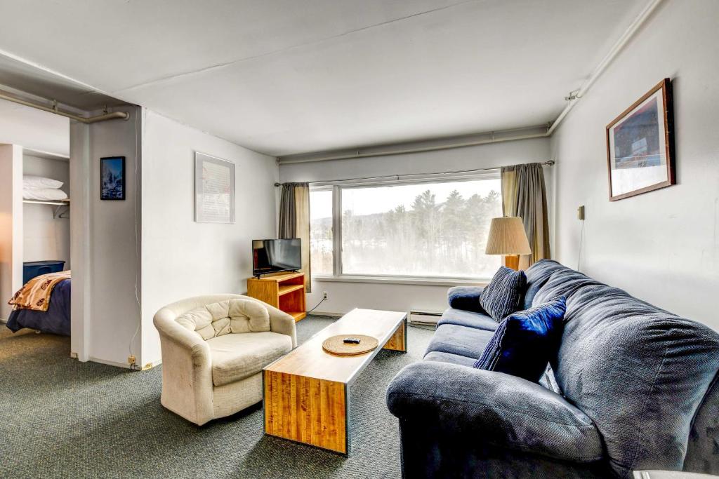 a living room with a blue couch and a table at Stowe Condo with Deck and Mountain Views! in Stowe