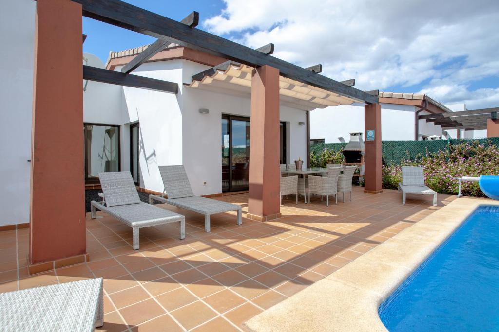 un patio con mesa y sillas y una piscina en Villa Rubi 19 Golf Private Pool Caleta de Fuste By Holidays Home, en Caleta de Fuste