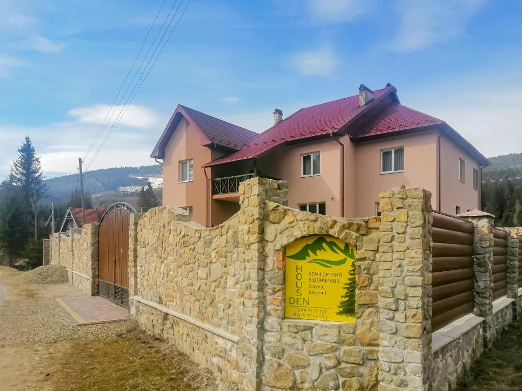 a house behind a stone wall with a sign at Den House in Myslovka