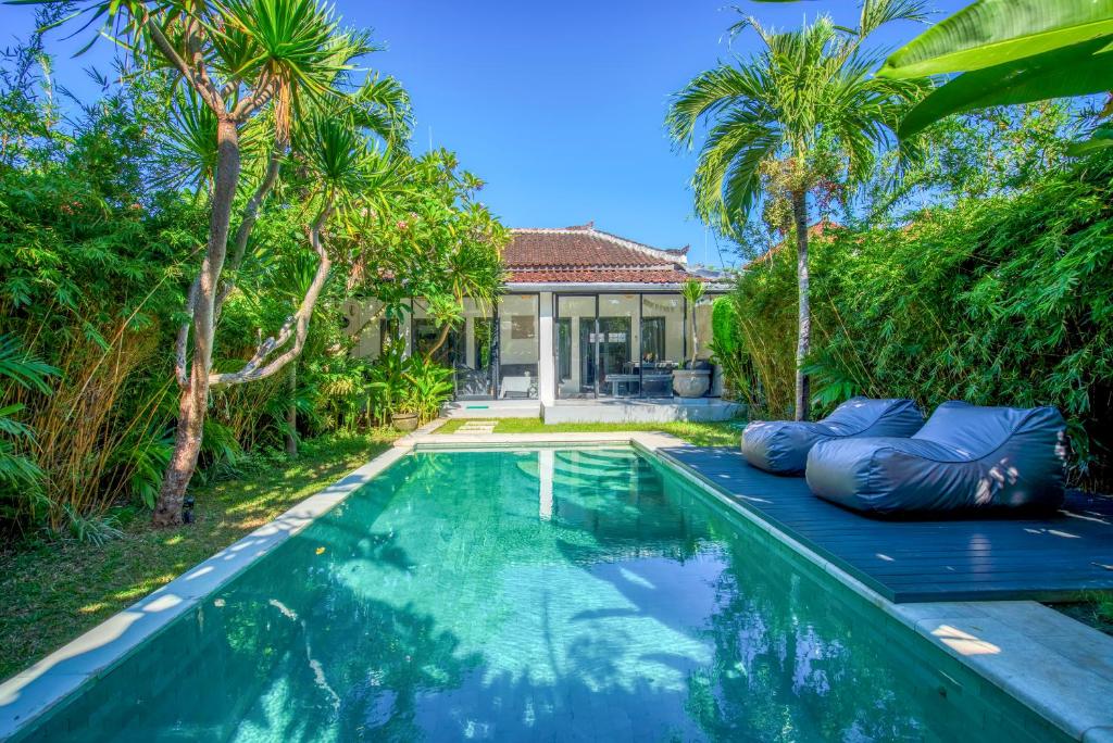 a swimming pool in a backyard with palm trees and a house at Villa Brezze - Nusa Dua in Nusa Dua