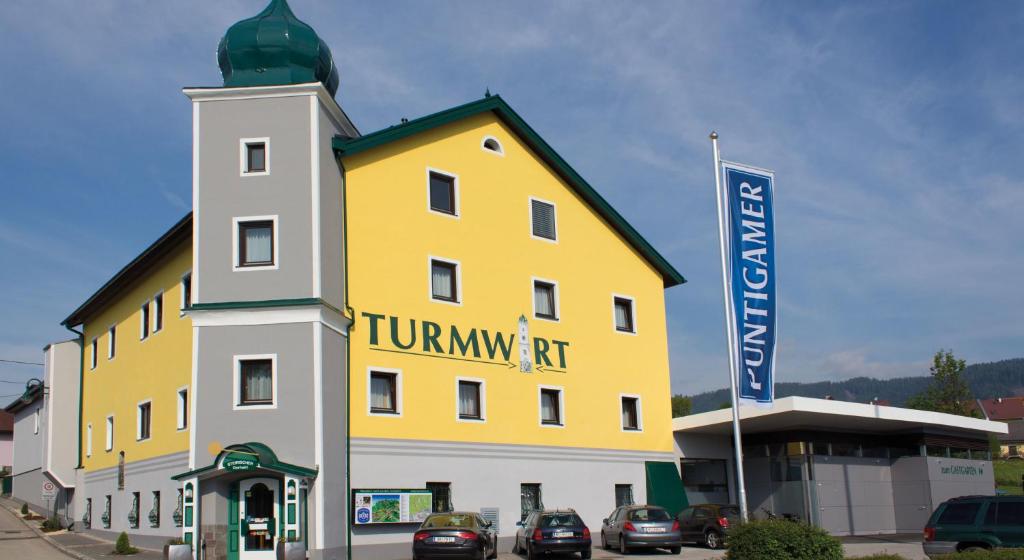 un edificio amarillo y blanco con coches estacionados frente a él en Gasthof Turmwirt, en Mürzhofen