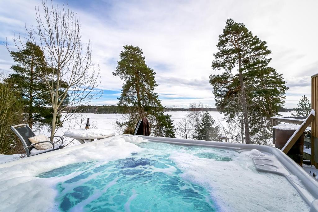 uma banheira de hidromassagem coberta de neve com vista para um lago em Relaxing Lake Oasis with Jacuzzi - Amazing view & Private Pier em Estocolmo