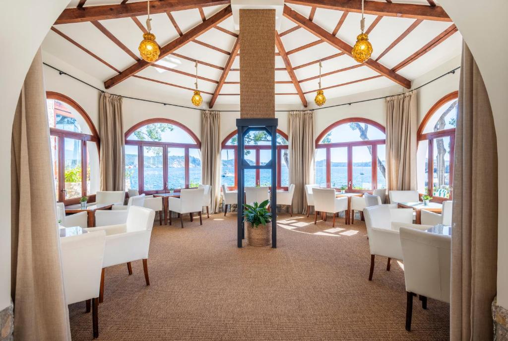 a dining room with white tables and chairs and windows at Hotel Cala Fornells in Paguera