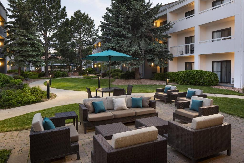 une terrasse avec des canapés, des tables et un parasol dans l'établissement Courtyard by Marriott Boulder, à Boulder