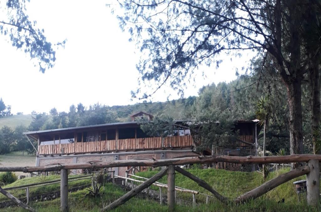 uma casa de madeira num campo ao lado de uma cerca em EL TRAPICHE em Sigchos