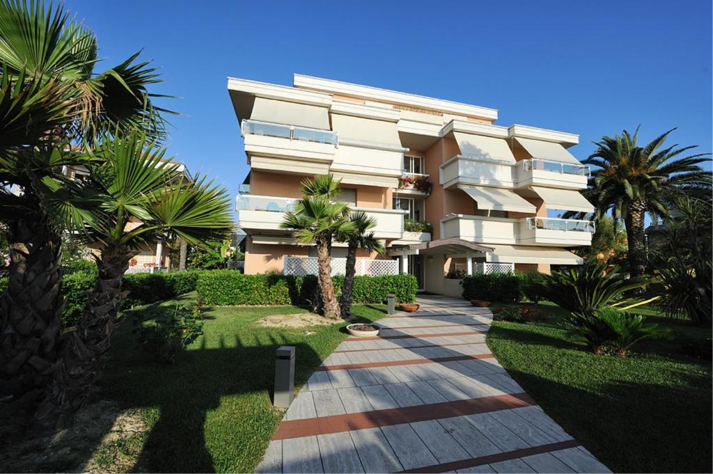 a building with palm trees in front of a walkway at Residence Le Palme in Grottammare