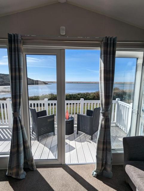 a living room with sliding glass doors with a view of the ocean at LOCATION LOCATION Beautiful Modern Frontline Caravan Haven Littlesea Weymouth in Weymouth