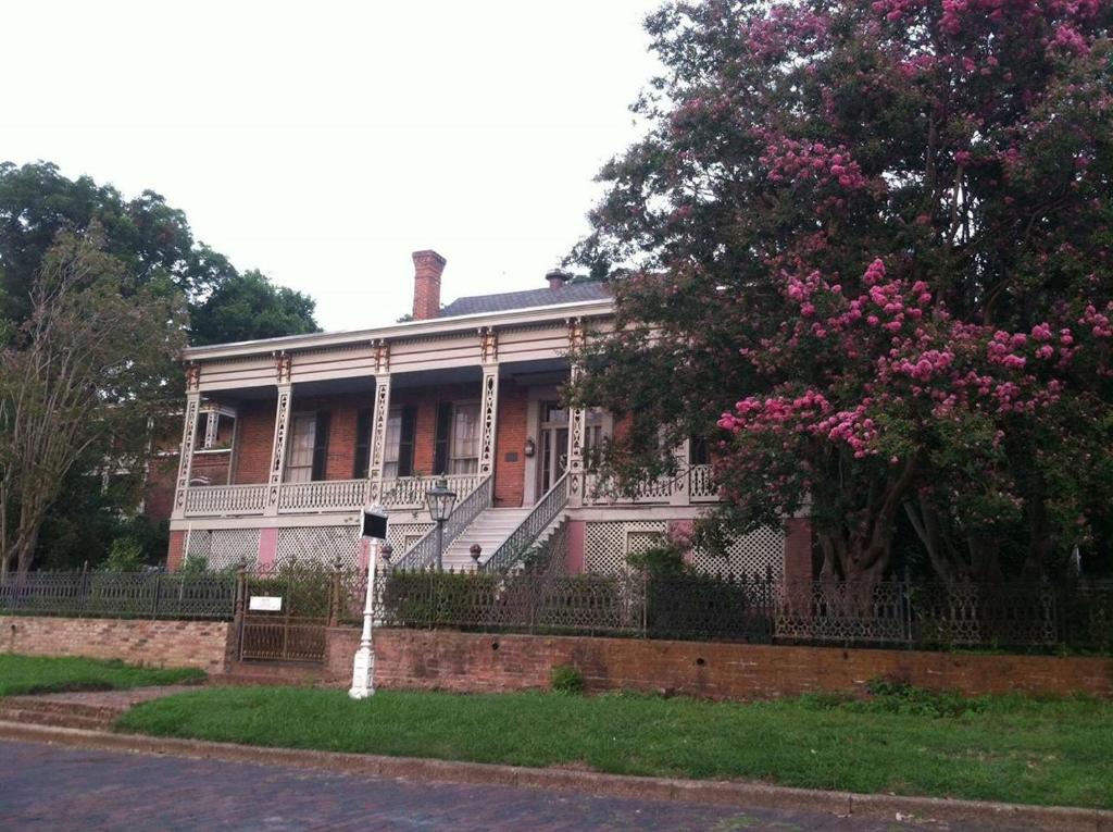 a house with a fence and a tree with pink flowers at Corners Mansion Inn - A Bed and Breakfast in Vicksburg