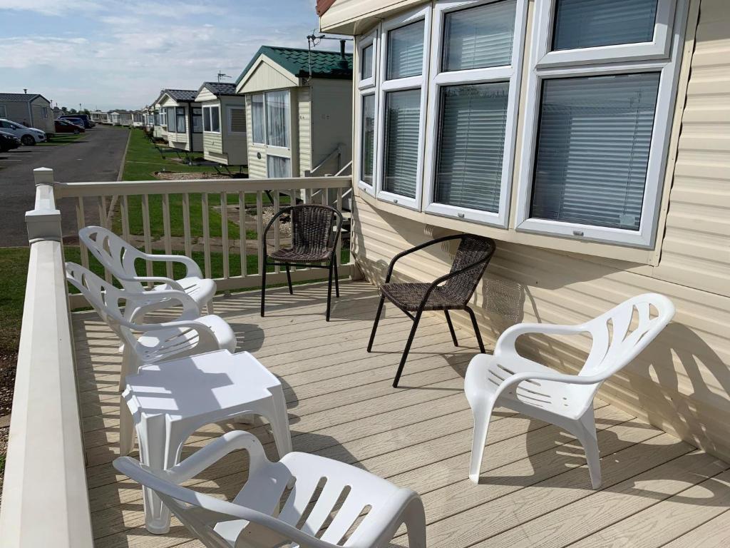 4 chaises blanches assises sur une terrasse couverte d'une maison dans l'établissement ST BREAKS BY THE BEACH, à Ingoldmells
