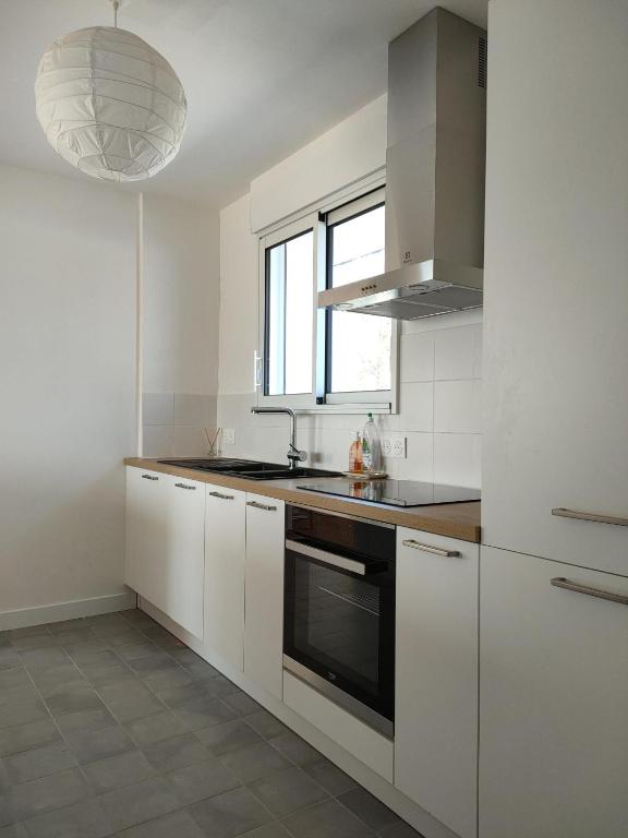 a kitchen with white cabinets and a sink and a window at Calme et lumière à 2 pas de la mer in Plouescat