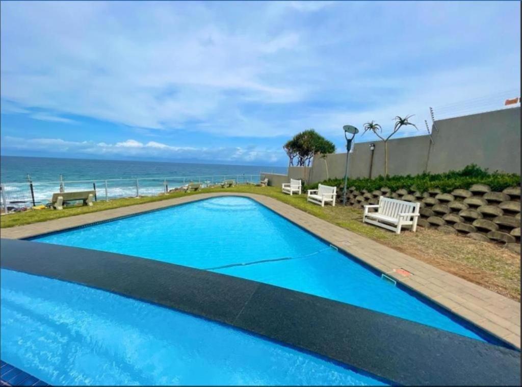 a blue swimming pool with the ocean in the background at Whale Rock, Modern Beachfront Apartment in Margate