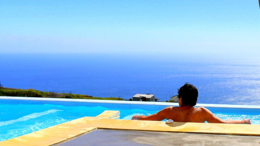 un hombre sentado en una piscina mirando el océano en Madeira Native Motion Guest House, en Fajã da Ovelha
