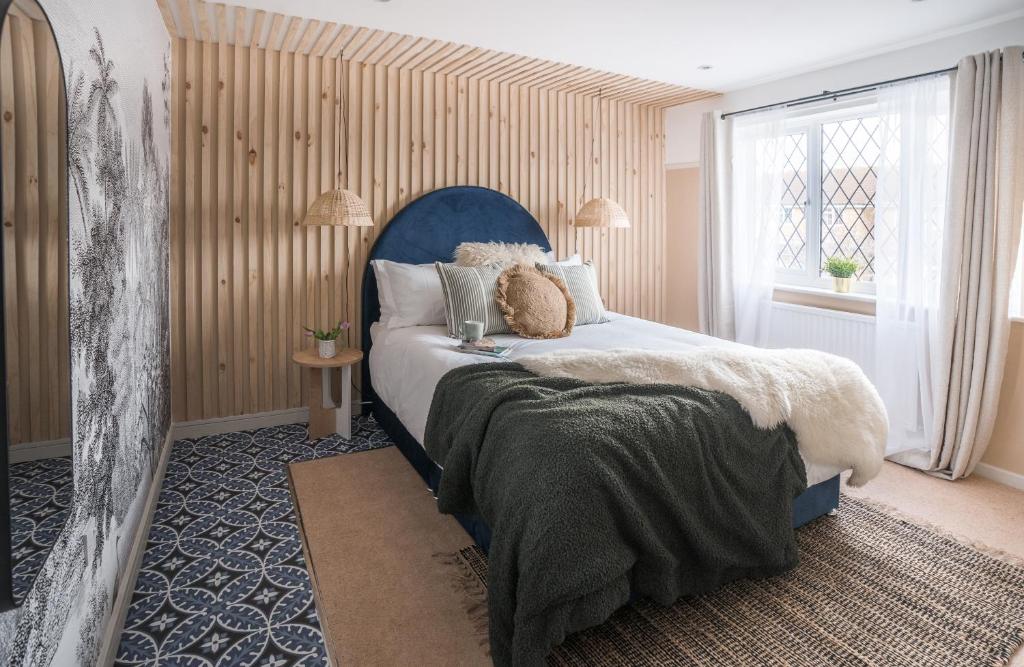 um quarto com uma cama com uma cabeceira azul e uma janela em 4-bed Cotswold getaway with hot tub & gaming room em Churchdown