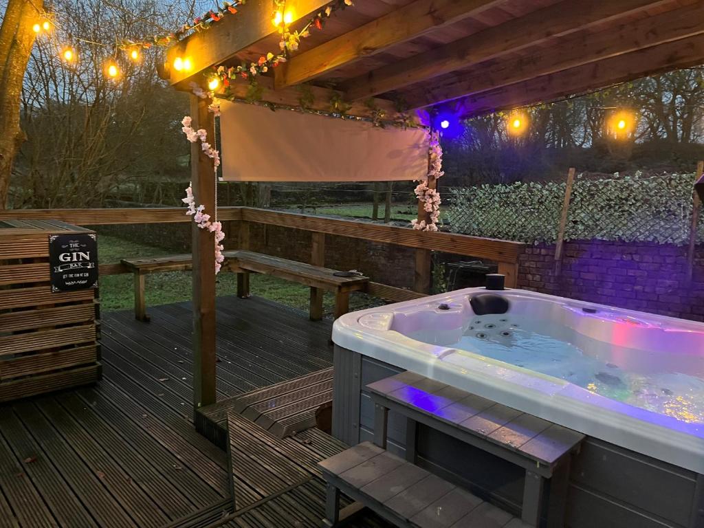 bañera de hidromasaje en una terraza con mesa de picnic y luces en The Cabin, en Bonnybridge