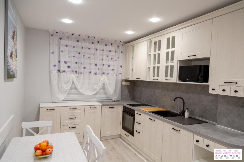eine Küche mit weißen Schränken und einem Tisch mit einer Schale Obst in der Unterkunft Rose Valley Aroma Apartment in Kasanlak