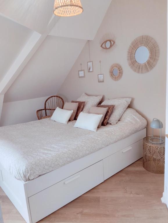 une chambre blanche avec un grand lit blanc avec des oreillers dans l'établissement Perle rare, appartement paisible et cosy, à Lamballe