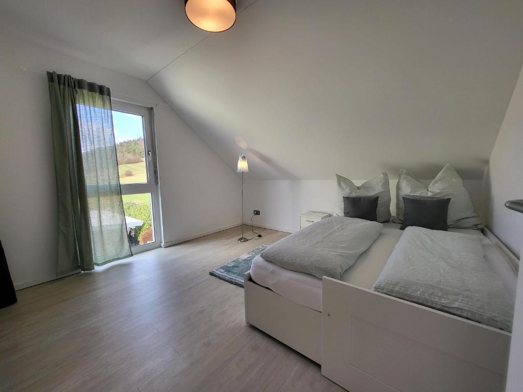 a white bedroom with a bed and a large window at Ferienwohnung Zartgrün Blumberg in Blumberg