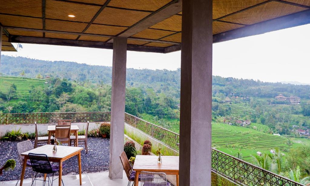 a balcony with tables and chairs and a view of a valley at Gunza Bed and Breakfast by BIJAK in Jatiluwih
