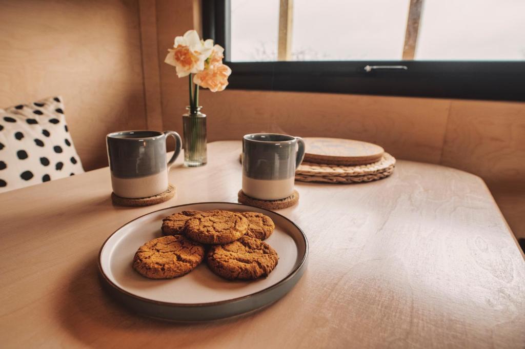 two cookies on a plate on a table with two cups at Luxury Glamping Cabin with Outdoor Bath on Cornish Flower Farm in Truro
