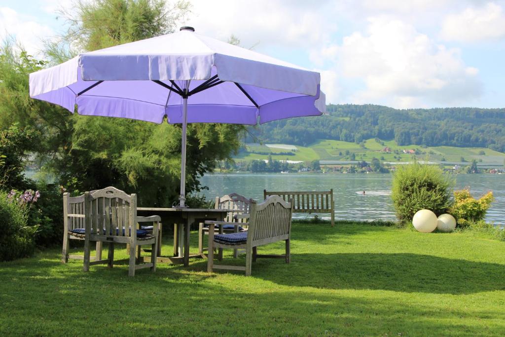 a picnic table with a purple umbrella and chairs at Gästehaus Stöhr - Ihre Ferienwohnungen mit großem Garten und direktem Seezugang in Öhningen
