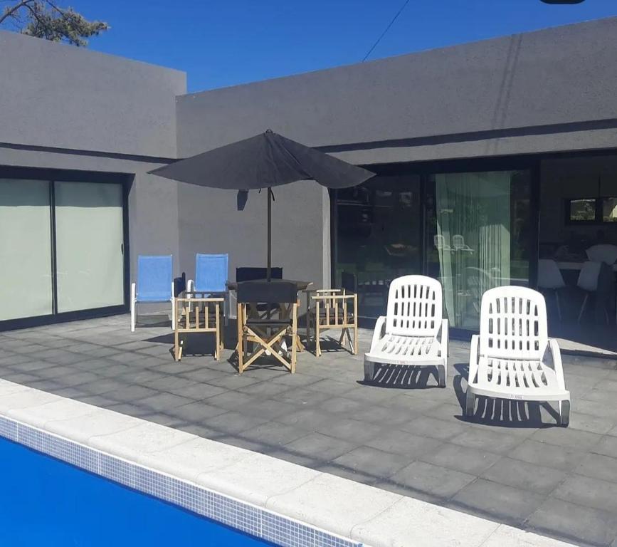 drei weiße Stühle und ein Regenschirm neben einem Pool in der Unterkunft Paraíso La Caleta in Mar de Cobo