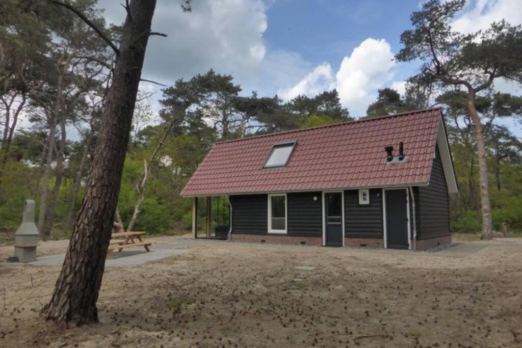 una pequeña casa con techo rojo y banco en het Beerzer Boshuis en Beerze