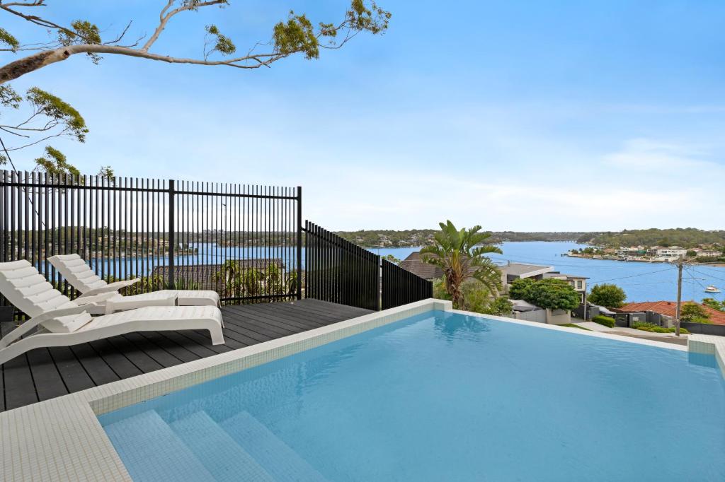 a swimming pool on a deck with chairs and the water at Luxury Waterside Home Sanctuary in Sydney