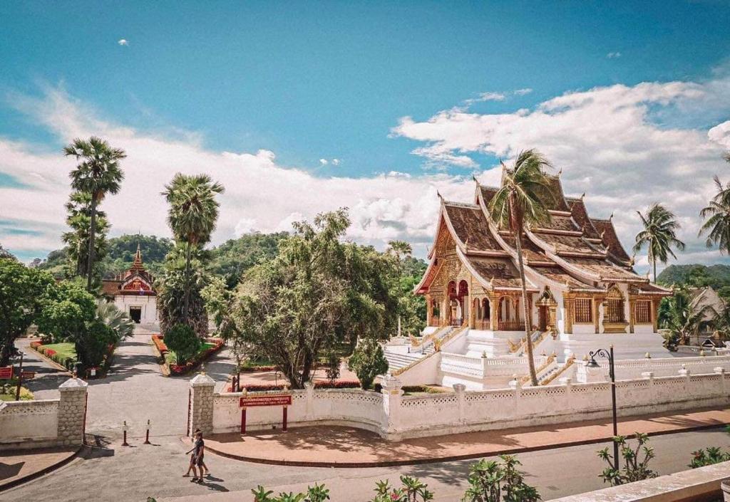a large building in a park with palm trees at Chaluenxay Xiengthong Place in Luang Prabang