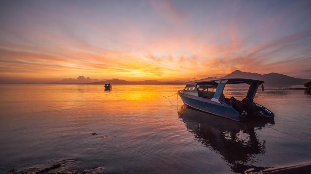 ein Boot, das bei Sonnenuntergang im Wasser sitzt in der Unterkunft Bunaken Sunrise Beach in Manado