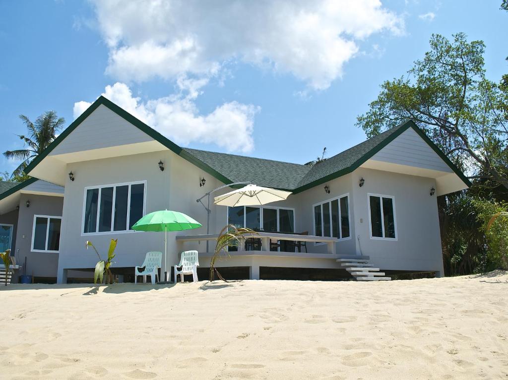 een wit huis met een parasol en stoelen op het strand bij The Moonrakers in Mae Nam