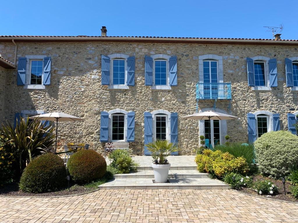 ein Steingebäude mit blauen Fensterläden und Büschen in der Unterkunft La Maison du Bonheur in Ausson