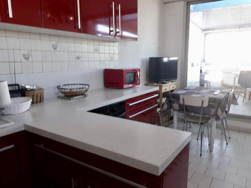 uma cozinha com um balcão branco e um micro-ondas vermelho em Appartement climatise - grande terrasse em Le Grau-du-Roi