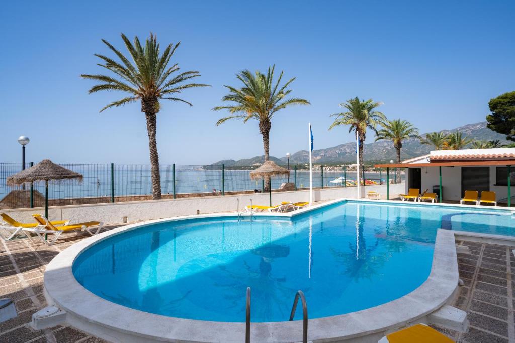 a large swimming pool next to a beach with palm trees at Medplaya Hotel Vistamar Costa Dorada in Hospitalet de l'Infant