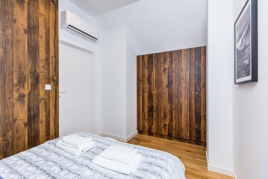 Cozy bedroom corner with wood-paneled wardrobe, air-conditioning unit, bed with folded towels.