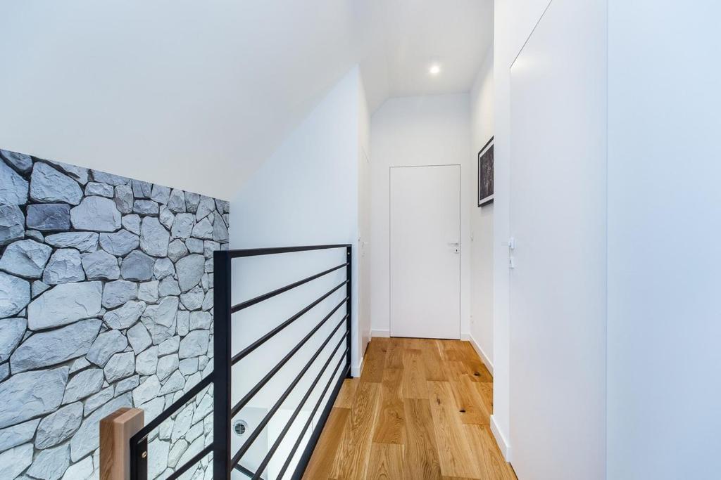 Bright upstairs hallway with black metal railing, stone accent wall, wooden floor, white door at end.