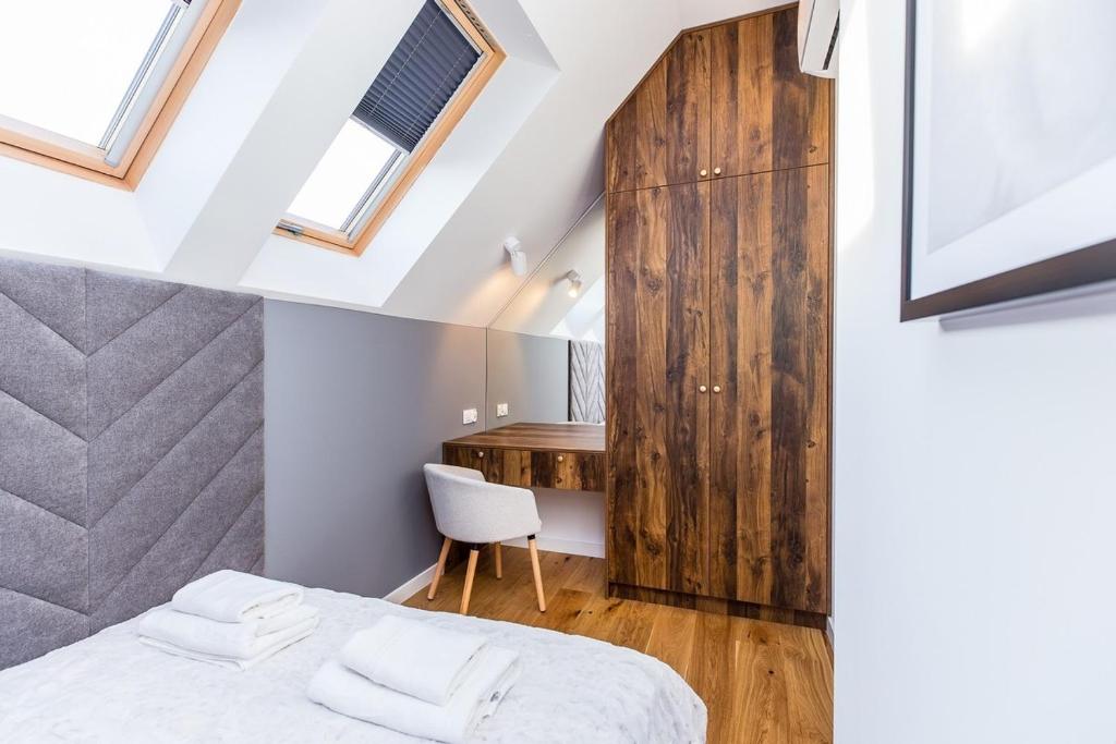 Attic bedroom with skylight windows, grey upholstered headboard, wooden desk and tall wardrobe.