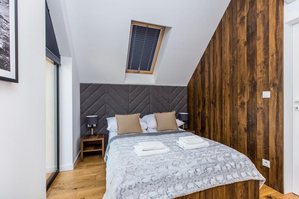 Bright bedroom with double bed, folded towels on blanket, grey headboard and wooden accent wall.