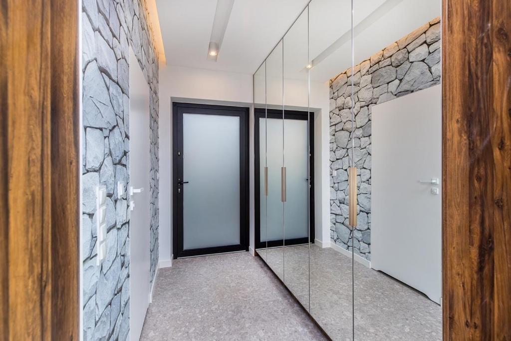Entry corridor with full-height mirrored closets, stone-patterned walls, frosted black door and wood trim.
