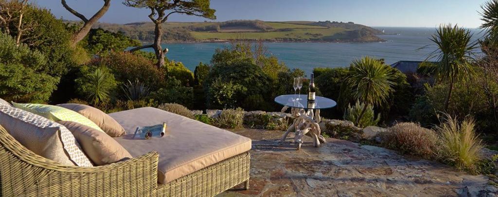 a wicker couch in a garden with a view of the ocean at Stargazers in Saint Mawes