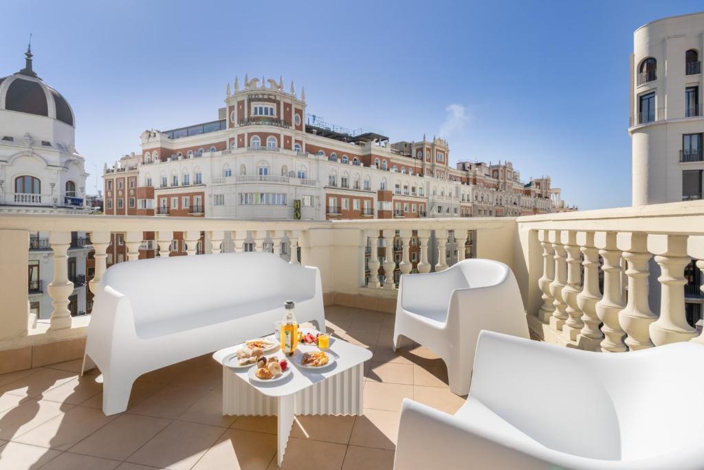 einen Balkon mit weißen Stühlen und einem Tisch mit Essen drauf in der Unterkunft Ikonik Gran Vía in Madrid