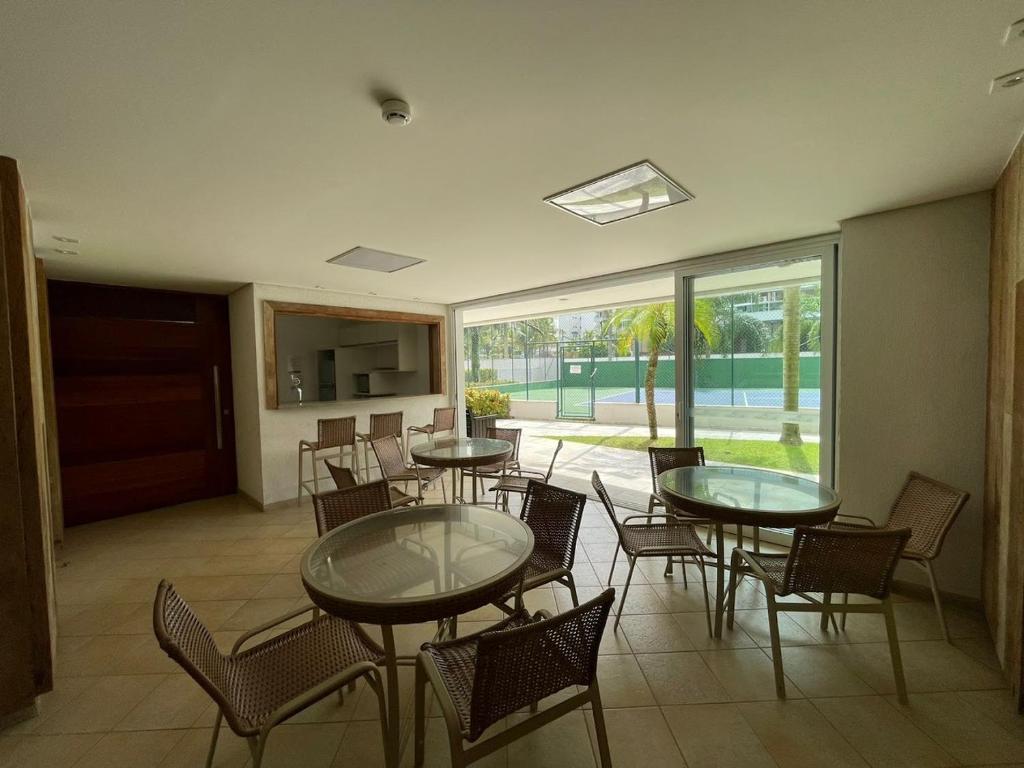 una sala da pranzo con tavoli, sedie e una grande finestra di Ilha da Madeira Resort Riviera de São Lourenço SP a Bertioga