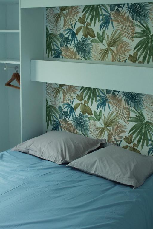 a bedroom with a blue bed with a tropical wallpaper at Les bungalows du chateau d'Ô in Petite Île