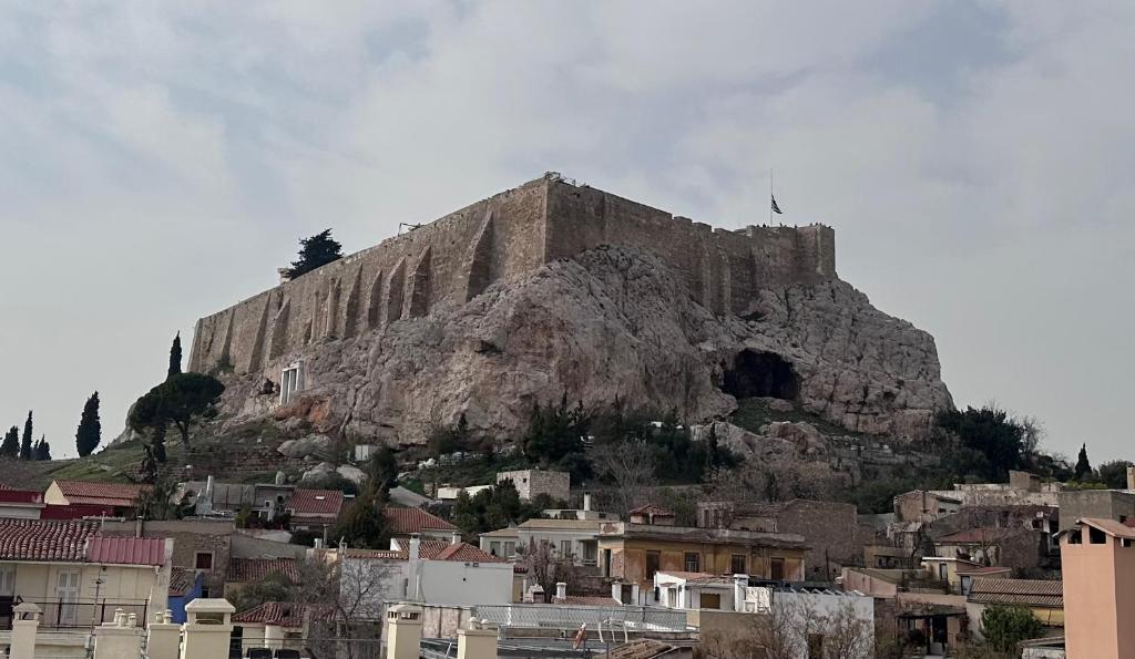 a large stone mountain with houses in front of it at Plaka With Acropolis Rooftop View Access in Athens