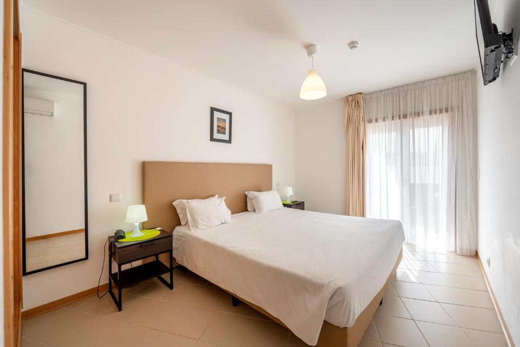 - une chambre avec un grand lit blanc et une fenêtre dans l'établissement Apartamentos Mirante da Rocha, à Portimão