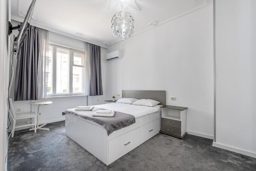 a white bedroom with a bed and a chandelier at Jazz & Wine - Luxury apARTment By The Sea & Parking & HBO & Netflix in Varna City