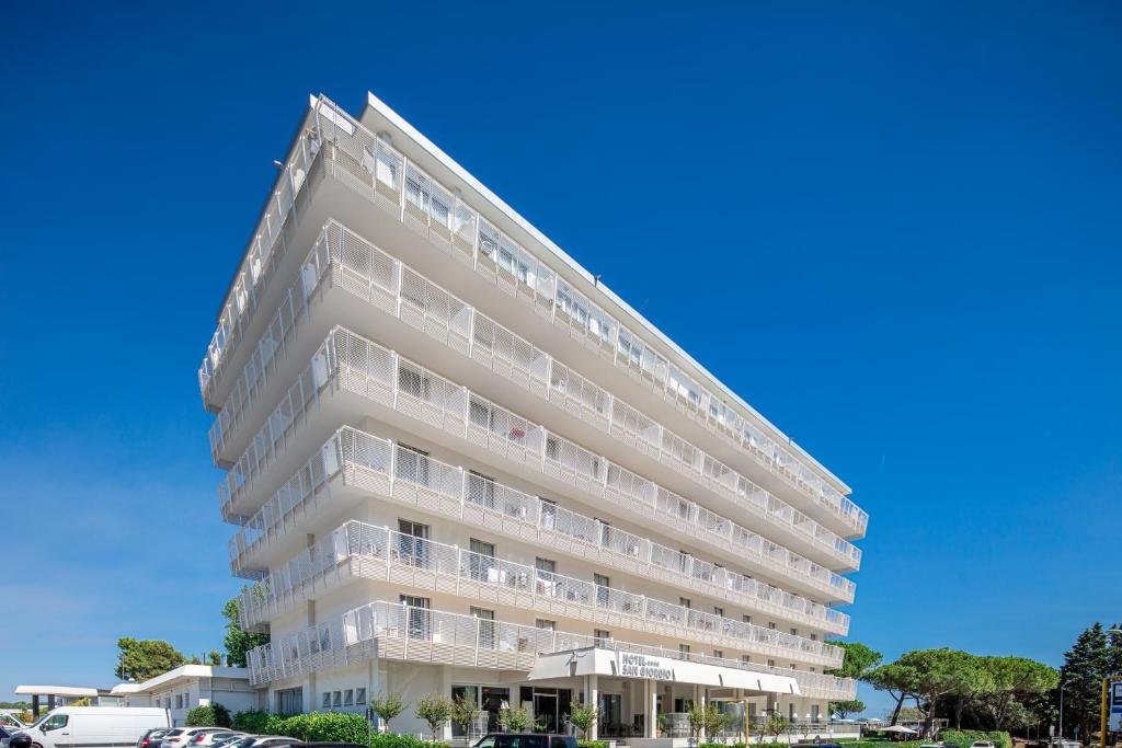 un edificio blanco alto con coches estacionados en un estacionamiento en Hotel San Giorgio, en Caorle