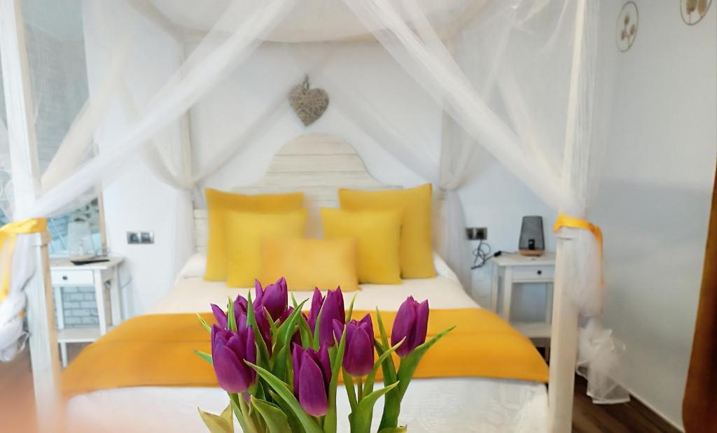 a bedroom with a bed with yellow pillows and purple flowers at Escapada Romantica con Jacuzzi y vistas al Castillo de Trevejo in Villamiel